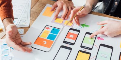 Cropped view of developers creative user experience design of mobile website with layouts on table