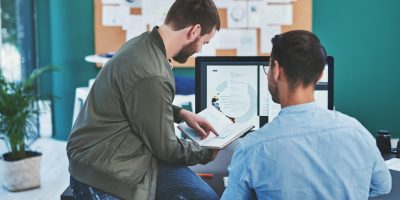 Office, men and meeting with diary for schedule for project deadline with planning and strategy as website designer. Back, male employees and coworking on meeting with teamwork and collaboration.