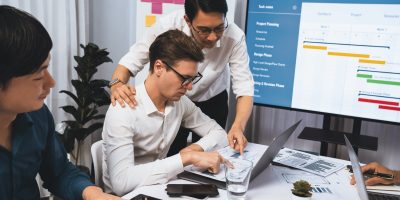 Project manager communicate and collaborate with team using project management software display on monitor, tracking progress of project task and making schedule plan at meeting table. Prudent